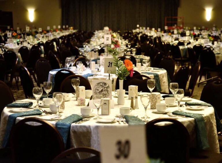 Rows of tables are set with plates, glasses, flowers, and other items in preparation for the annual Mayors Dinner event
